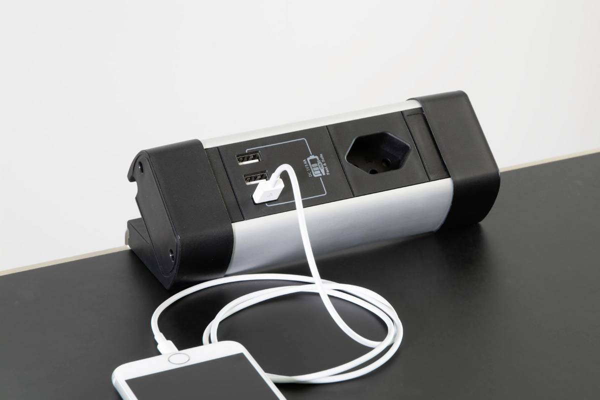 Une prise de table avec des ports USB. Un smartphone est connecté à l'un des ports USB de la prise via un câble de charge.