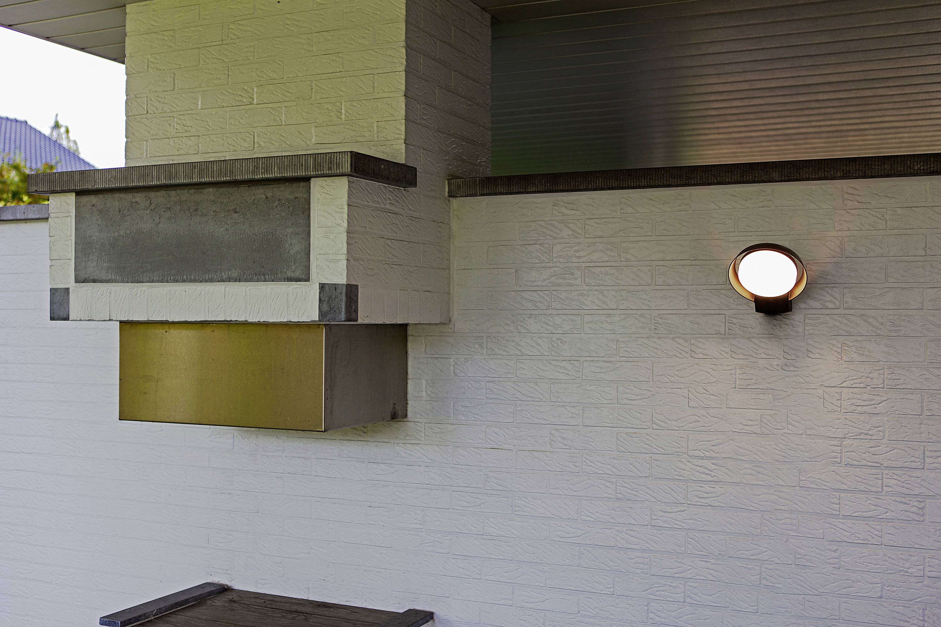 Vue extérieure d'une cheminée moderne avec une applique murale ronde sur un mur de briques blanches. La cheminée est équipée d'un conduit de cheminée en métal.