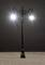 Un lampadaire en fer forgé avec deux lampes illuminées sur un fond sombre.