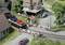 Scène de train miniature avec un passage à niveau et plusieurs voitures, incluant un train de marchandises chargé de véhicules. Une petite maison à colombages se trouve en arrière-plan.