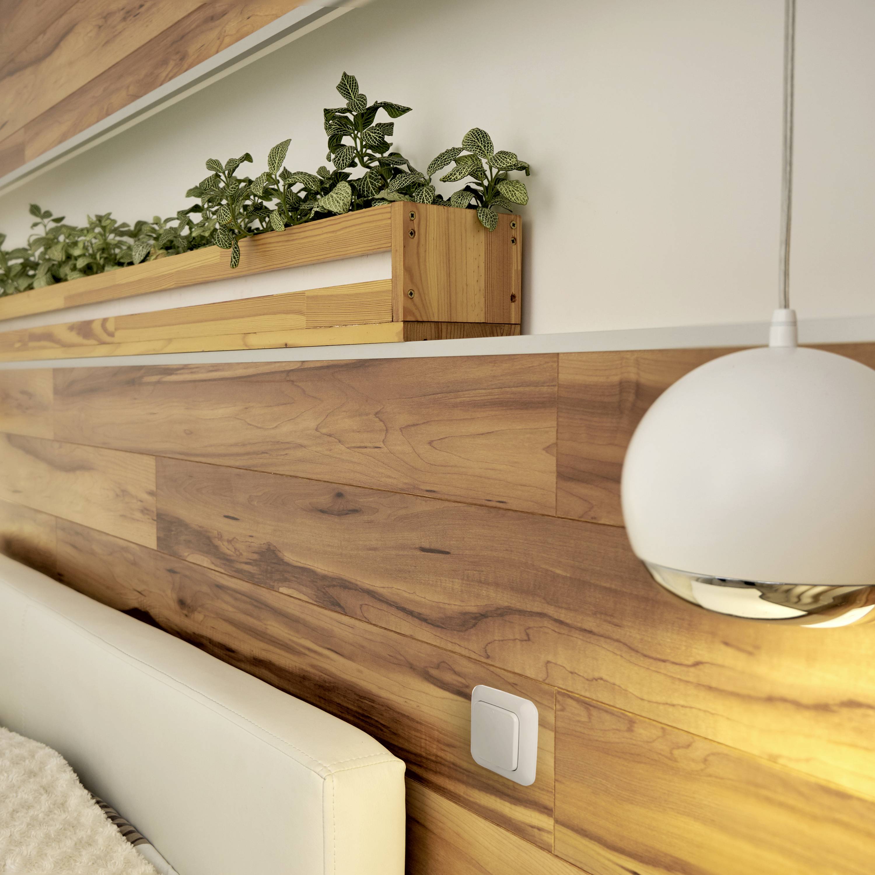 Chambre à coucher moderne avec lambris en bois et meubles en bois pâle. Un jardinière fixée au mur avec des plantes vertes.