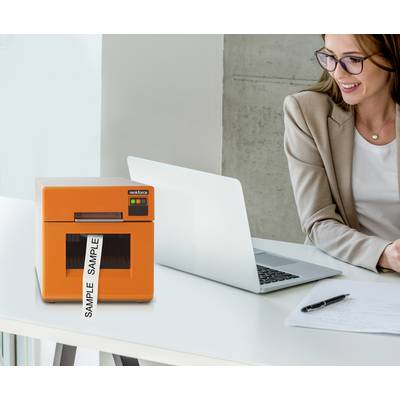 Une femme est assise à un bureau avec un ordinateur portable, un bloc-notes et un stylo. Une imprimante orange avec une étiquette 'SAMPLE' est posée à côté.