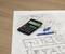 Une table avec un plan architectural, une calculatrice et des stylos, symbolise la planification et le calcul dans le domaine de la construction.