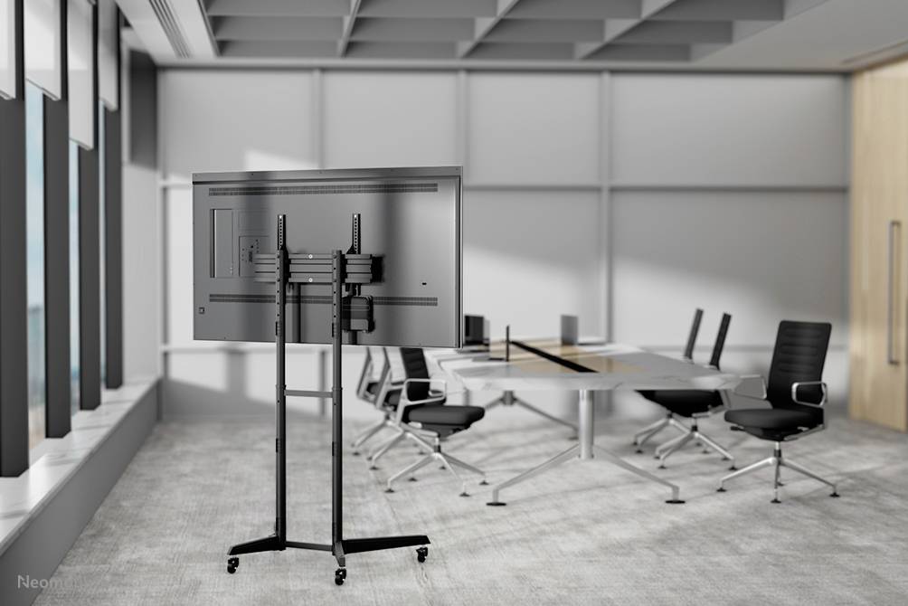 Une salle de conférence équipée d'un grand écran sur un support mobile. Une table rectangulaire est entourée de chaises modernes.