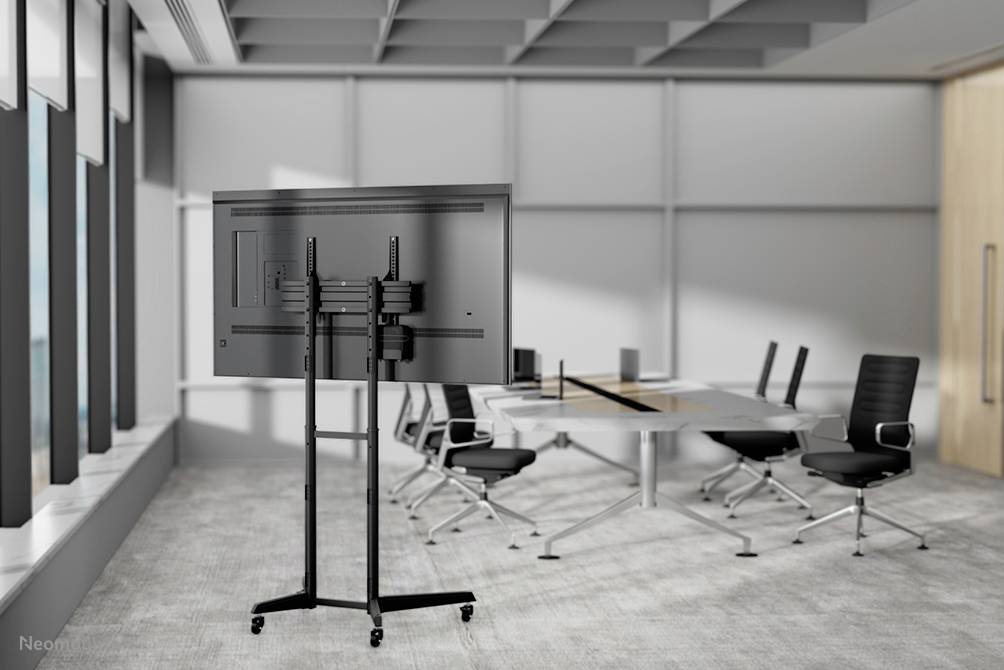 Salle de conférence moderne avec un grand écran sur support, une table et des chaises noires. Une grande fenêtre apporte de la lumière naturelle.