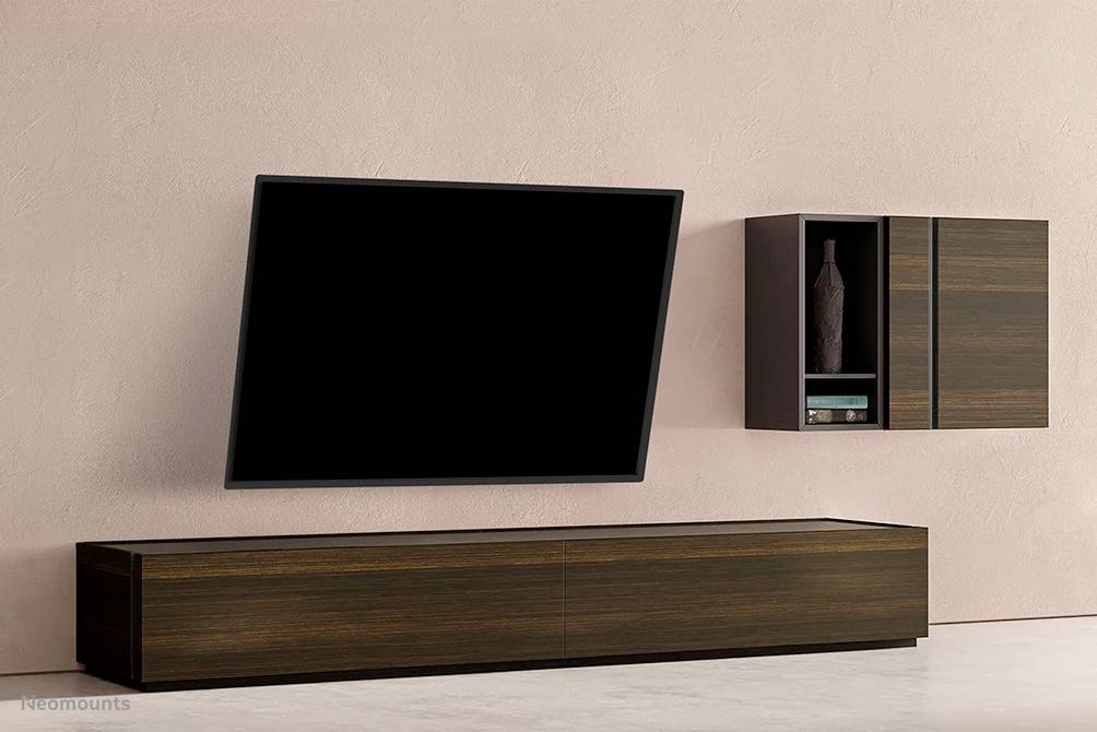 Un téléviseur moderne est suspendu en biais sur un mur rose. En dessous se trouve une étagère plate en bois foncé. En haut à droite, une petite étagère murale.