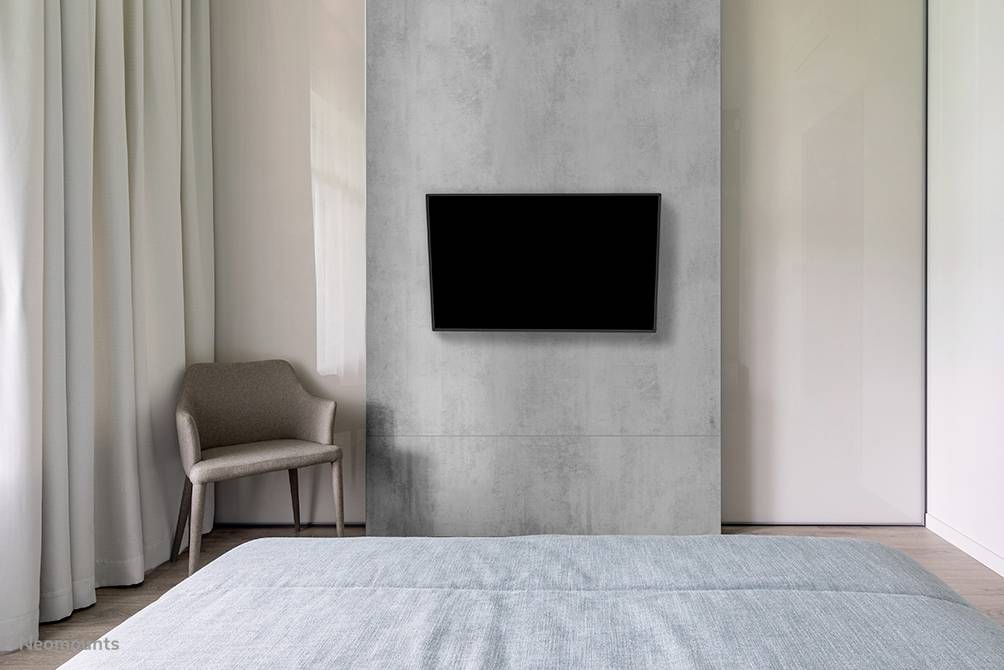 Téléviseur à écran plat fixé à un mur en béton dans une chambre moderne aux couleurs neutres avec une chaise.