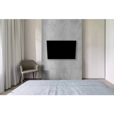 Une chambre moderne avec un accent de béton gris sur le mur, sur lequel est monté un grand téléviseur plat noir. Une chaise est placée à gauche.