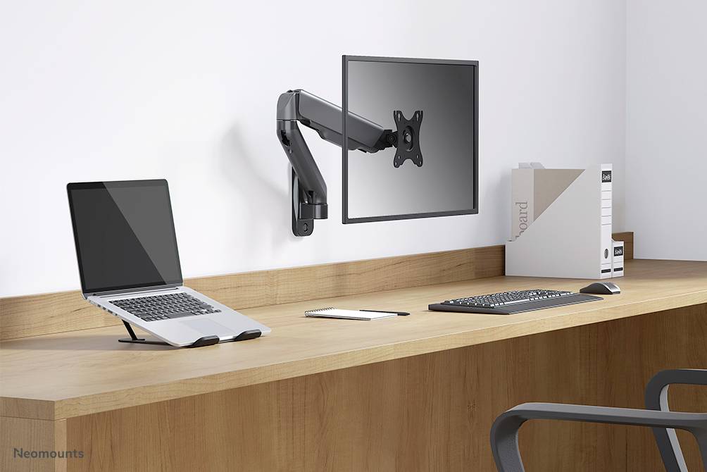 'Poste de travail moderne avec un ordinateur portable, écran sur bras pivotant, clavier et souris sur une table en bois. Classeurs de documents en arrière-plan.'