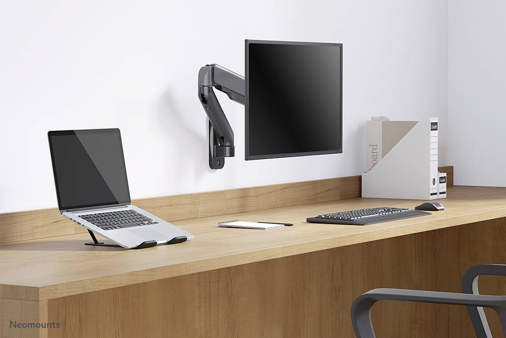 Bureau avec un ordinateur portable sur support, écran monté, clavier, souris et classeurs. Espace de travail moderne dans une pièce lumineuse.