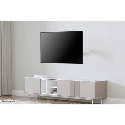Un téléviseur plat moderne est accroché au mur au-dessus d'un meuble TV blanc minimaliste dans une pièce lumineuse.
