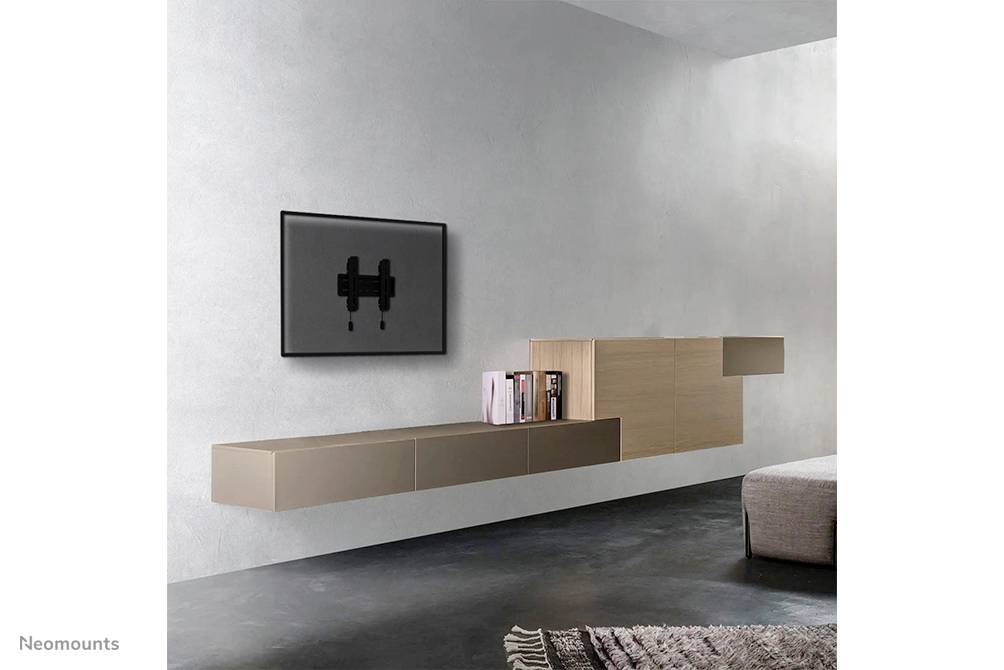 Un salon minimaliste avec un mur gris. Un téléviseur plat est monté au mur, à côté duquel se trouvent des étagères flottantes garnies de livres.