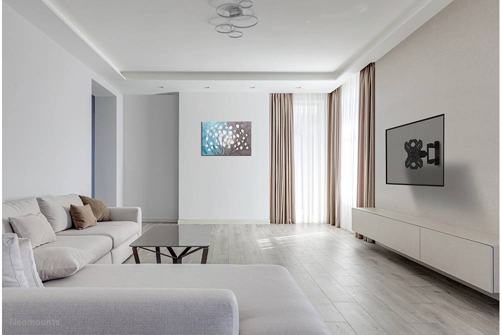 Salon lumineux aux murs blancs, avec un canapé gris, une table basse et un tableau sur le mur à gauche. Un téléviseur est placé à droite sur un meuble TV bas.