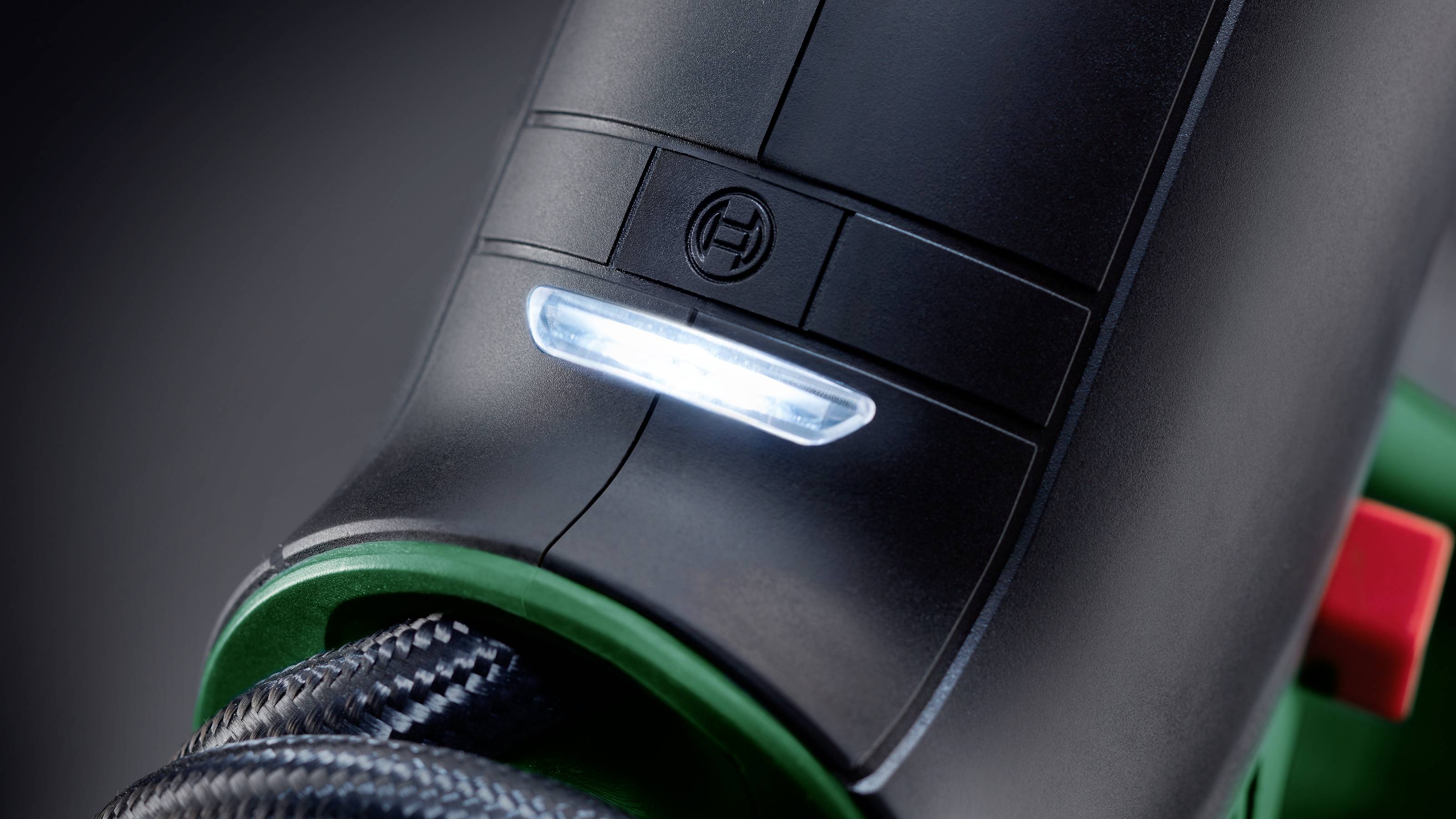 Gros plan d'un appareil noir avec une LED illuminée et un câble tressé, probablement un outil électrique ou un appareil électroménager.
