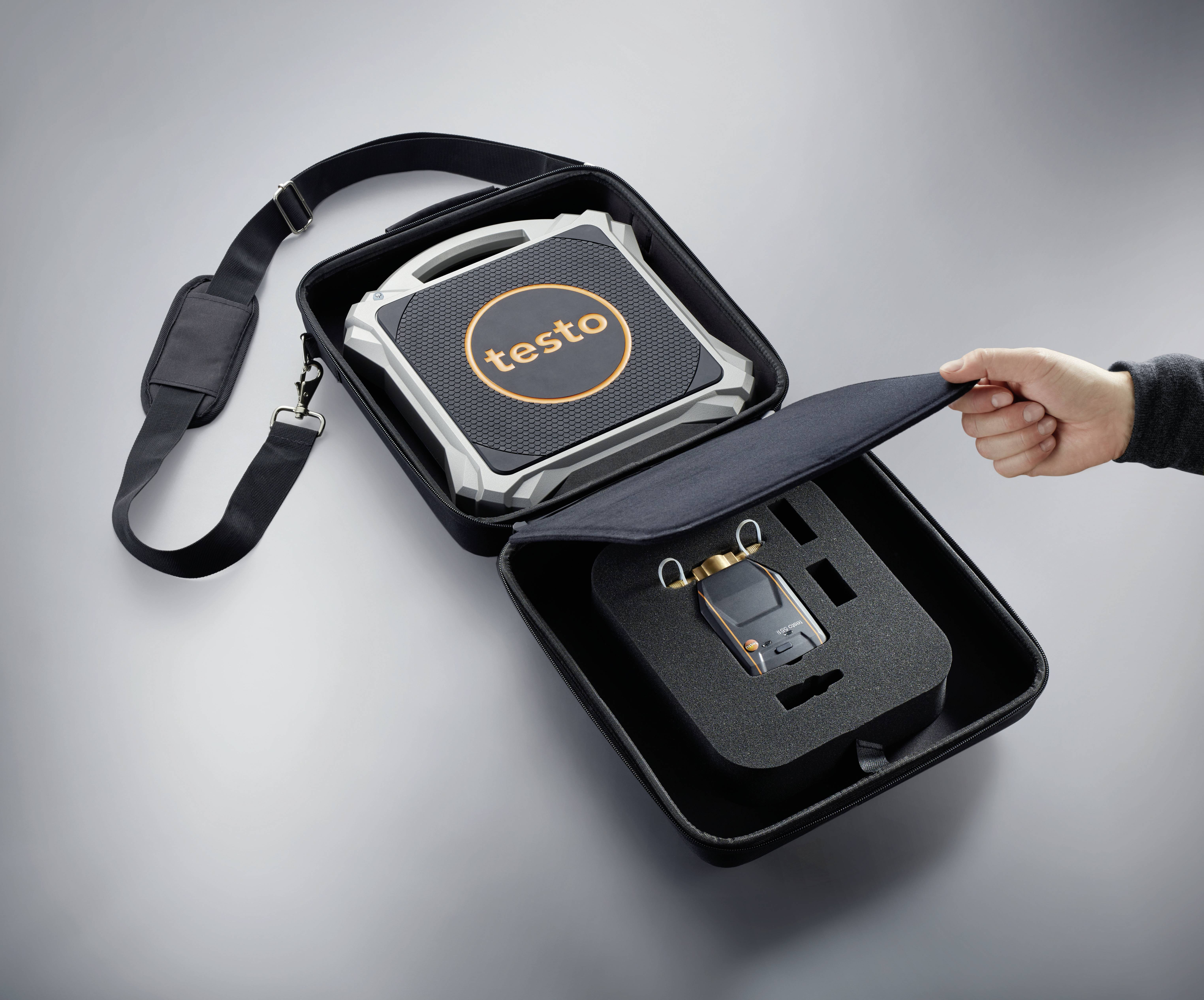 Une main ouvre un sac noir contenant un appareil de mesure et ses accessoires, à l'intérieur duquel un dispositif de Testo est clairement visible.