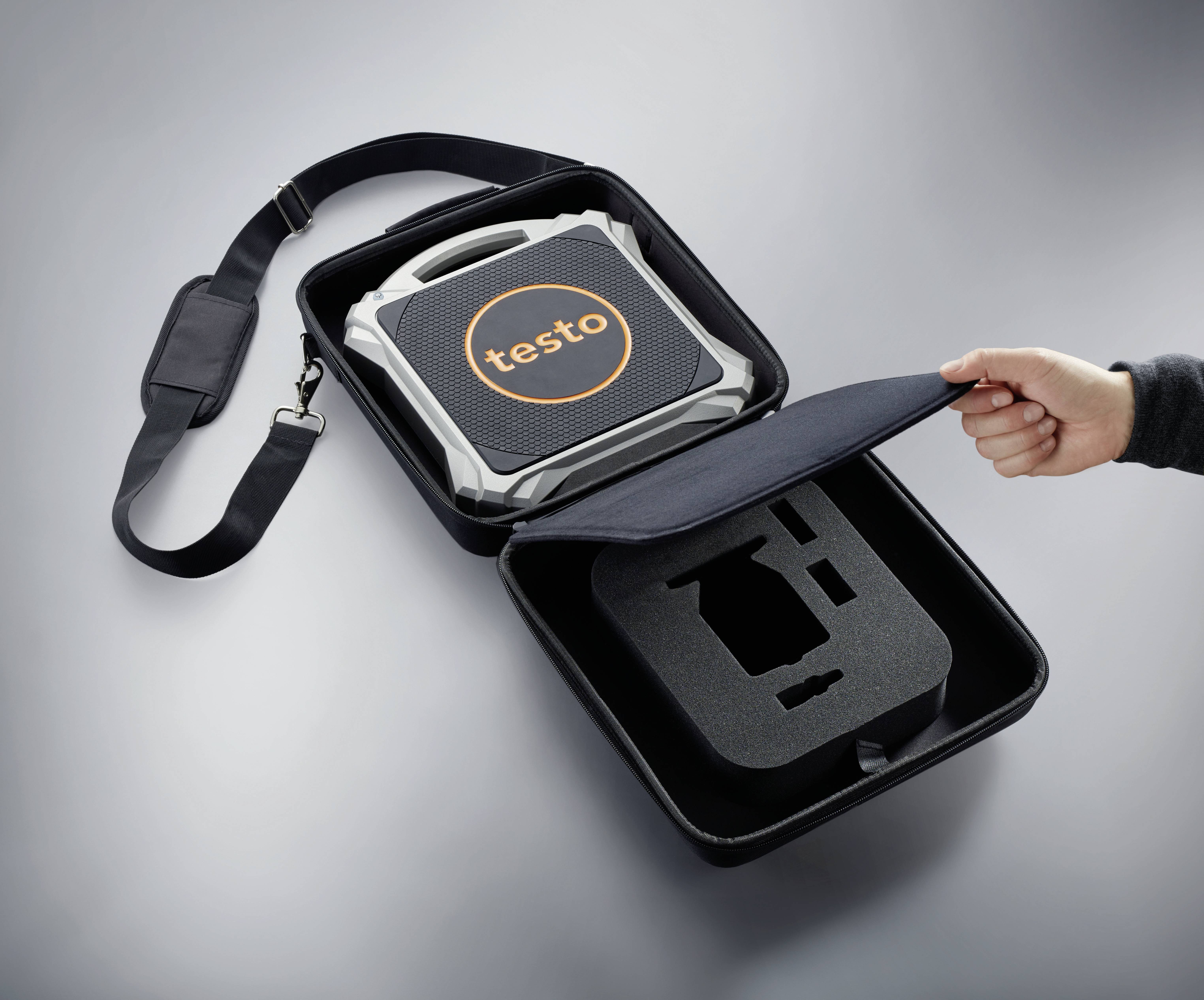 Une main ouvre un sac de transport contenant un appareil portant l'inscription 'testo'. L'appareil est sécurisé dans un cadre de mousse protectrice.
