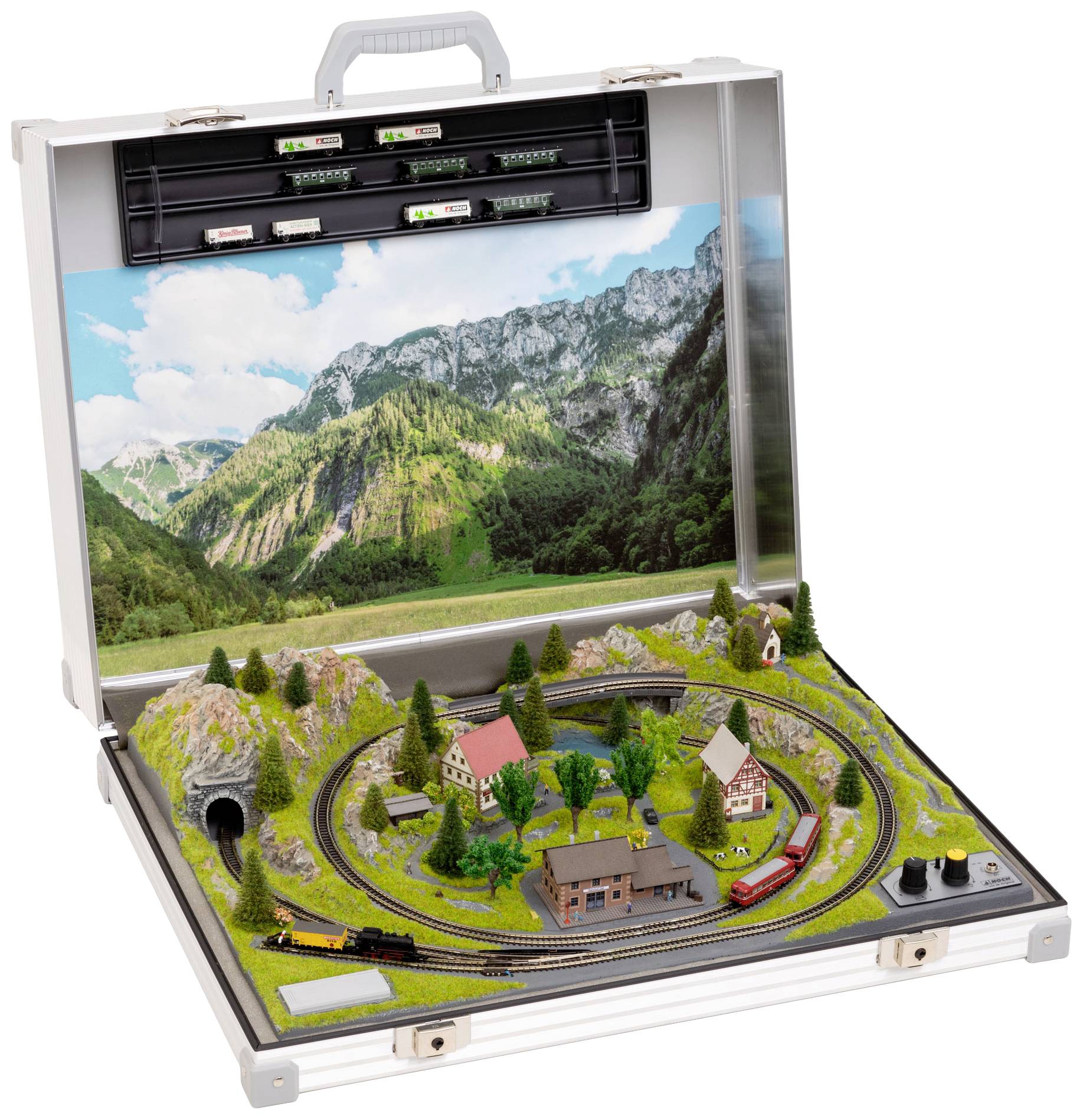 Une valise ouverte révèle un paysage ferroviaire miniature avec des montagnes, des arbres, des maisons et deux trains, entouré de paysages verdoyants.