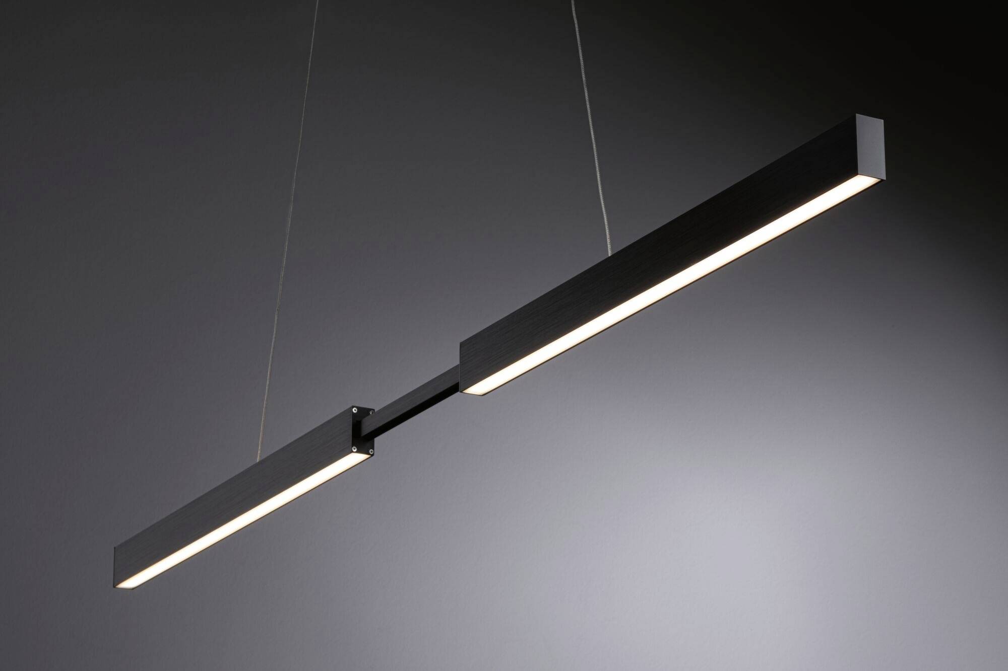 Une suspension LED moderne en noir au design étroit et rectangulaire, suspendue par deux câbles devant un fond gris.