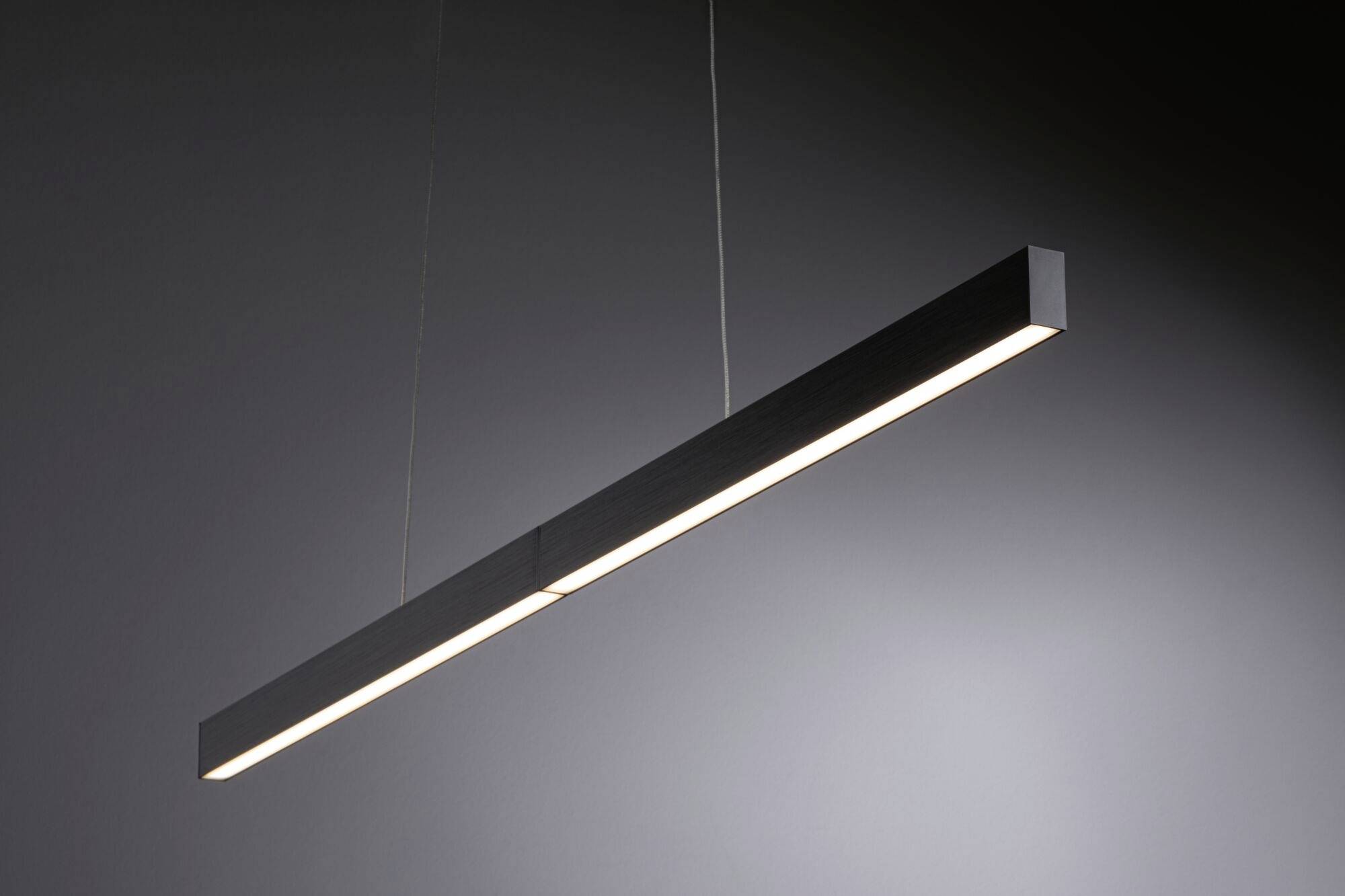 Une suspension simple, noire, est suspendue au plafond. Elle a une forme longue et rectangulaire et éclaire uniformément la pièce.