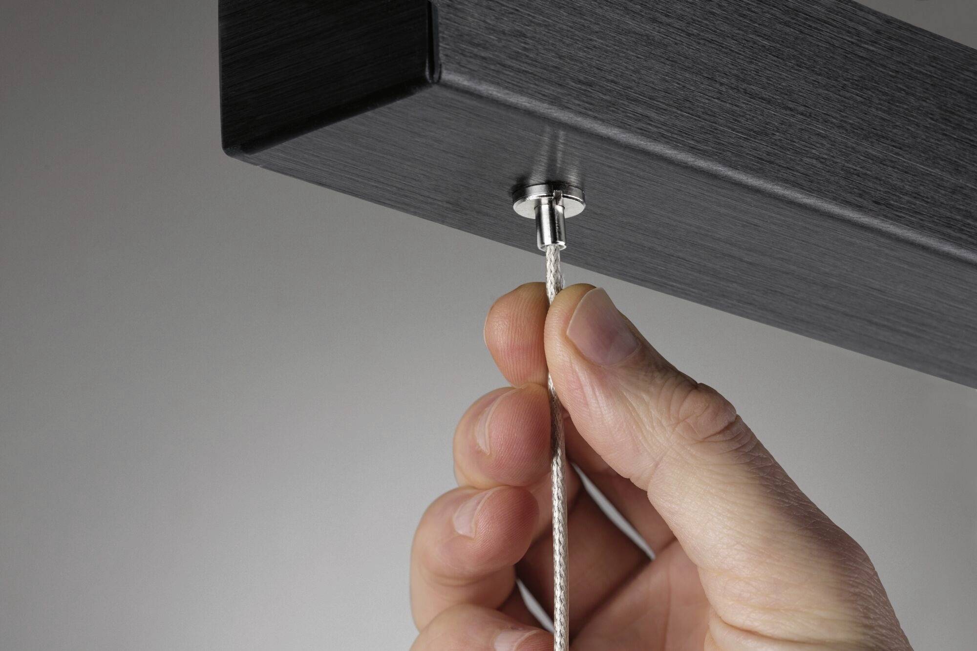Une main tire doucement sur une corde attachée à une pièce métallique rectangulaire et sombre.