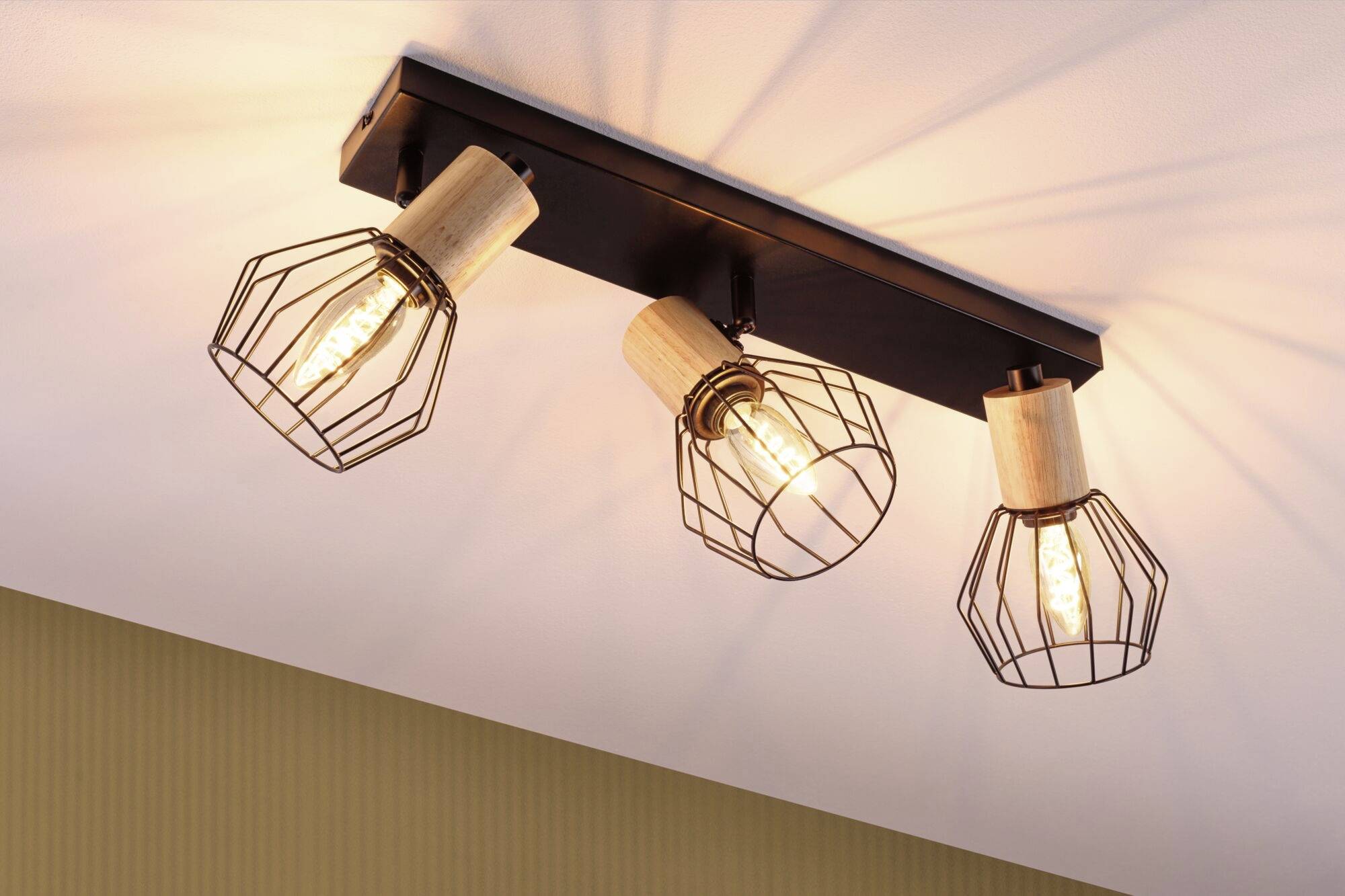 Trois luminaires modernes au plafond avec des grilles métalliques autour des ampoules, montés sur un support en bois, diffusent une lumière chaleureuse.