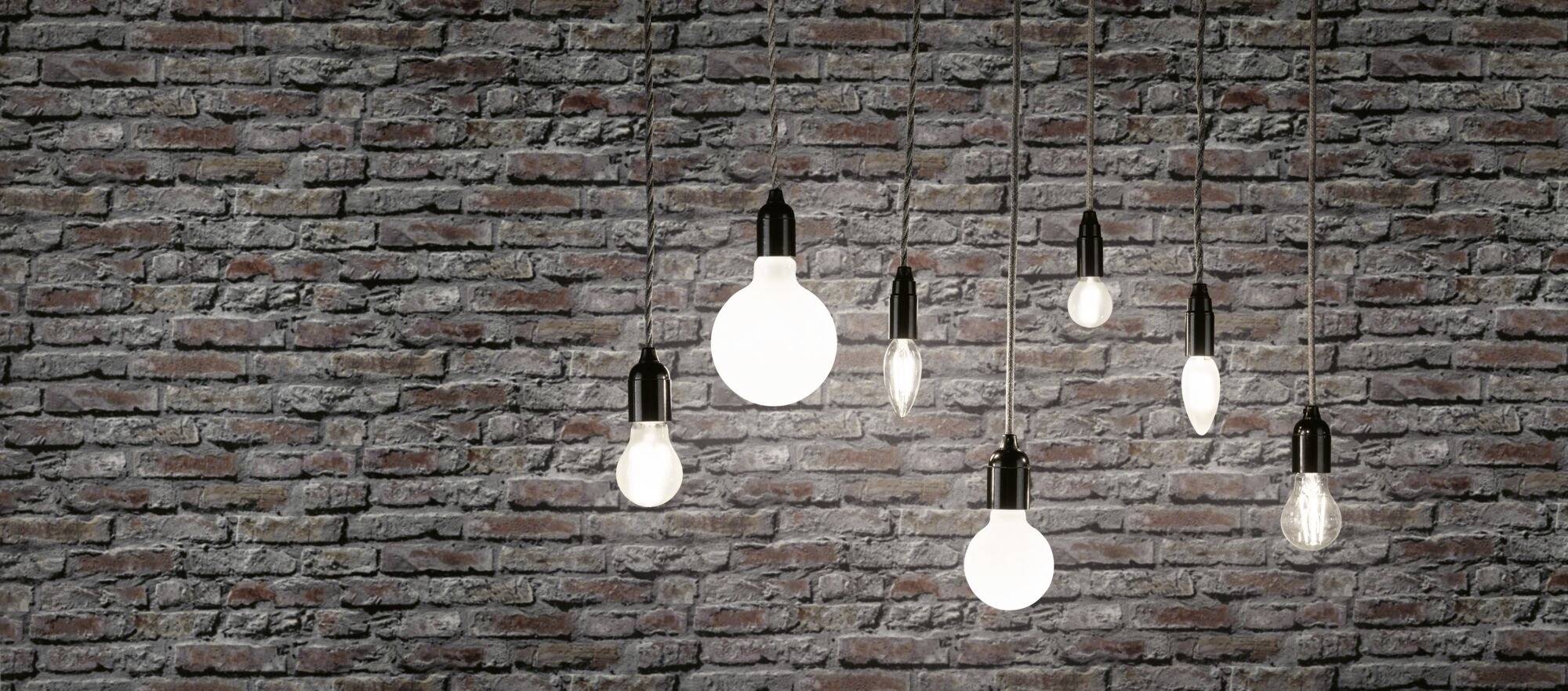Plusieurs ampoules sont suspendues devant un mur de briques et illuminent la pièce avec des intensités différentes.