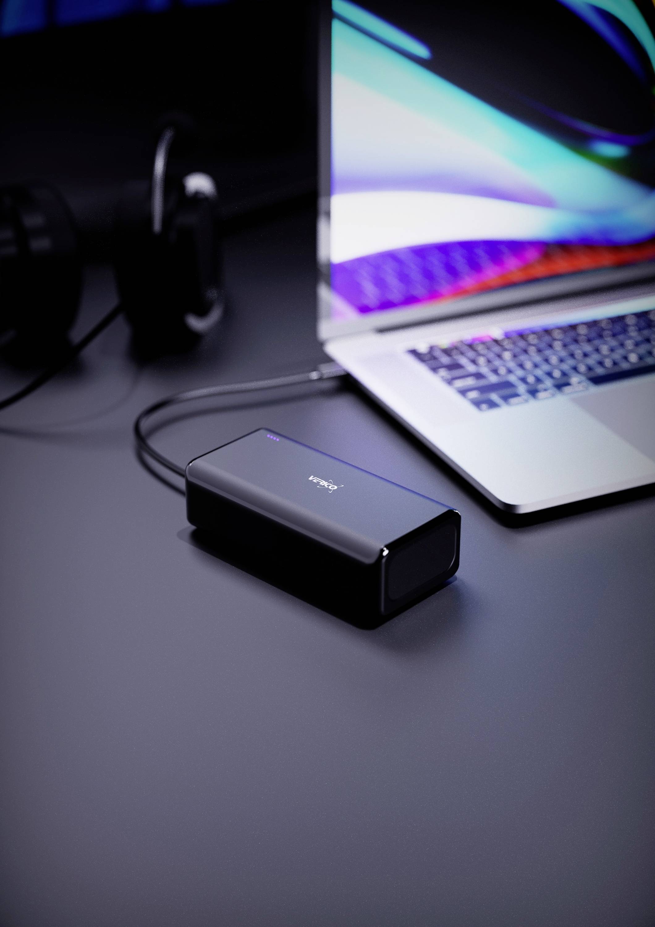 Un ordinateur portable avec un écran coloré est posé sur une table. À côté se trouve un périphérique externe, probablement un disque dur, connecté à l'ordinateur portable.