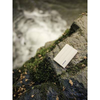 Disque dur externe avec aspect bois posé sur une pierre recouverte de mousse au bord d'un ruisseau coulant dans une forêt.