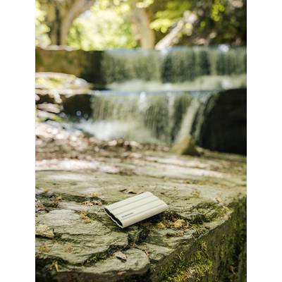 Un petit carnet blanc est posé sur un rocher au premier plan, avec une cascade naturelle dans la forêt en arrière-plan.