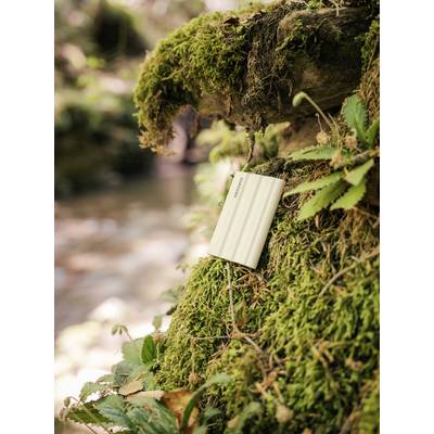 Un chargeur portable est appuyé contre un tronc d'arbre couvert de mousse dans une forêt, symbolisant une technologie durable au sein de la nature.