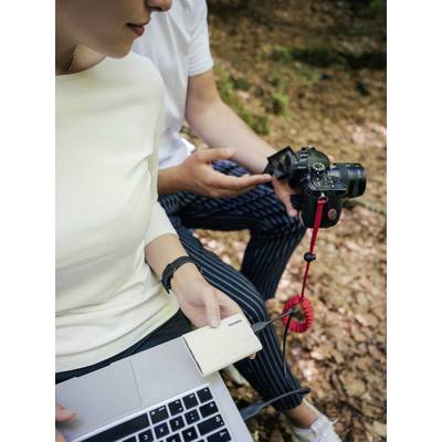 Une personne tient un appareil photo, tandis qu'une autre personne transfère des données d'un périphérique de stockage vers un ordinateur portable.