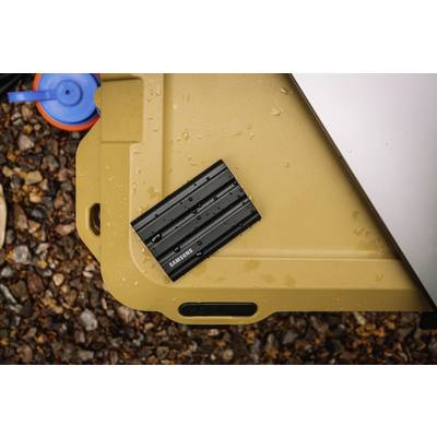 Un disque dur externe noir, résistant à l'eau, de la marque 'Samsung' est posé sur un fond beige à l'extérieur.