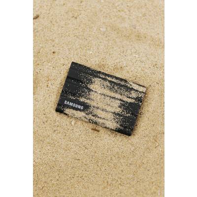 Un disque dur noir de Samsung est posé dans le sable. Il est partiellement recouvert de sable sur le dessus.
