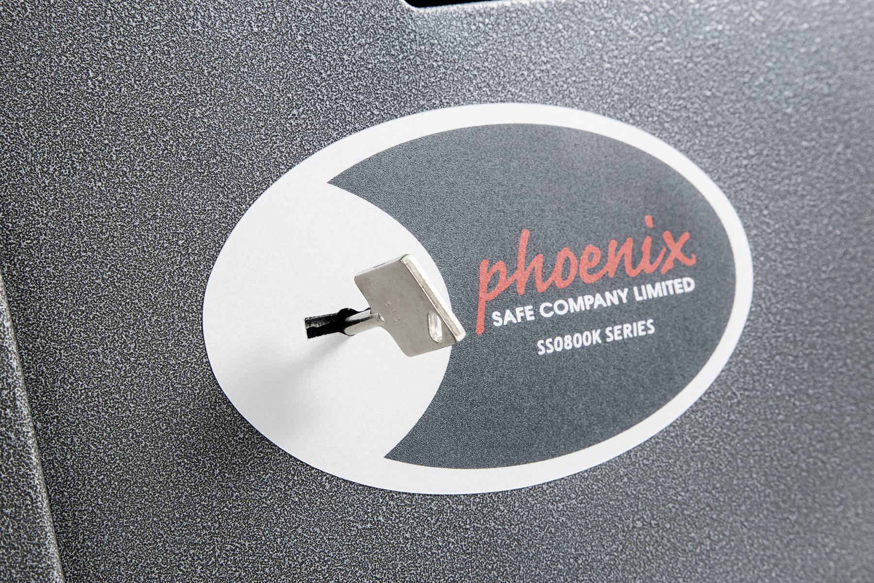 Un trou de serrure avec une clé insérée se trouve sur un coffre-fort de la marque 'phoenix', modèle 'SS0800K SERIES'.