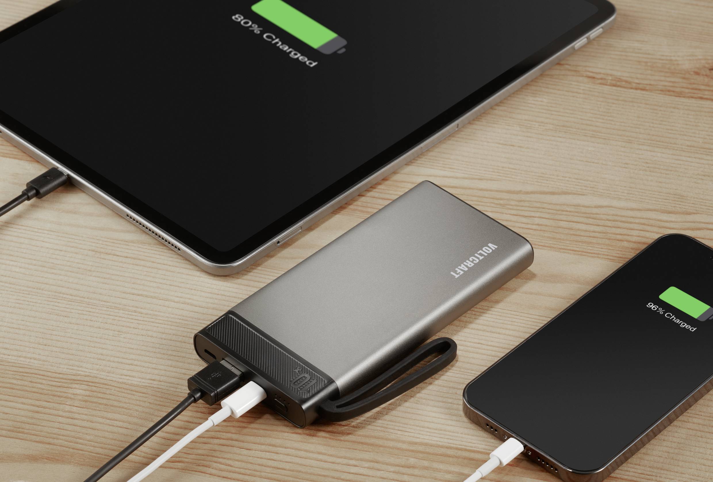 Une tablette et un smartphone sur une table en bois, connectés à une batterie externe, affichant tous deux « 80% chargés ».