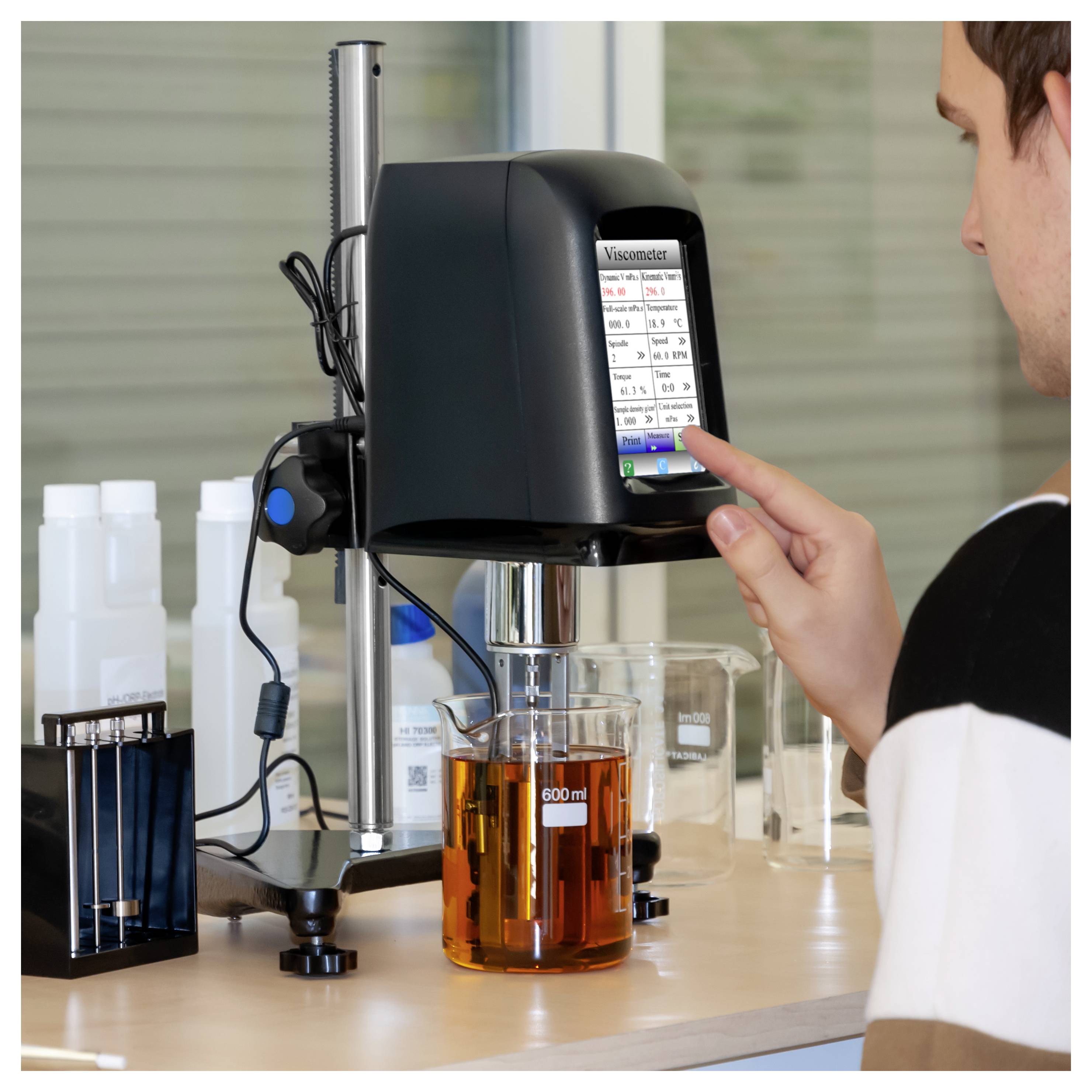 Personne utilisant un viscosimètre sur un banc de laboratoire, avec un bécher de liquide ambré sous l'instrument et des récipients de laboratoire à proximité.