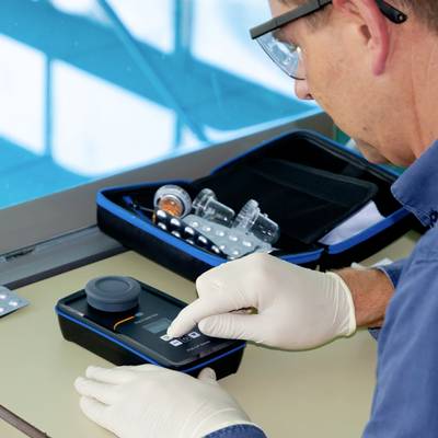Une personne portant des gants de laboratoire utilise un photomètre portable sur une table. Des équipements et des solutions de laboratoire sont visibles en arrière-plan.