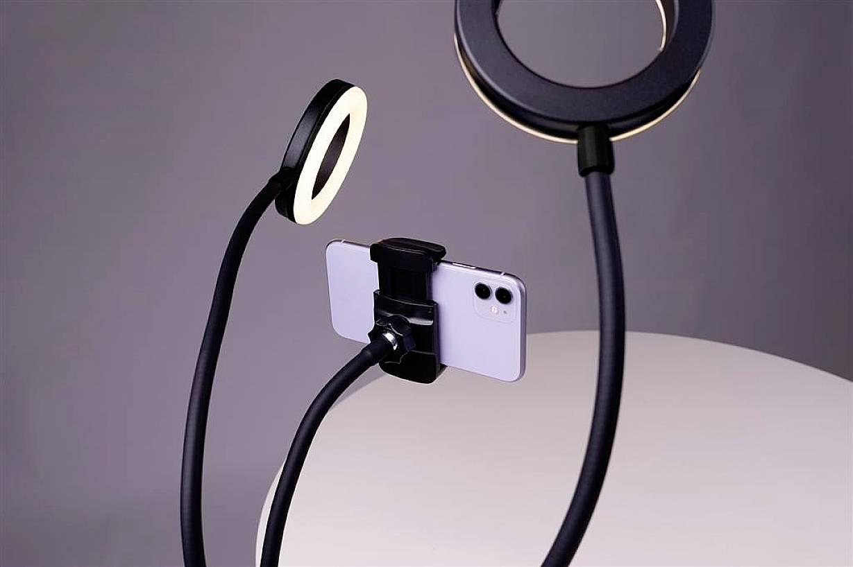 Smartphone sur support flexible entre deux anneaux lumineux, adapté aux enregistrements vidéo ou aux selfies avec un éclairage optimal.