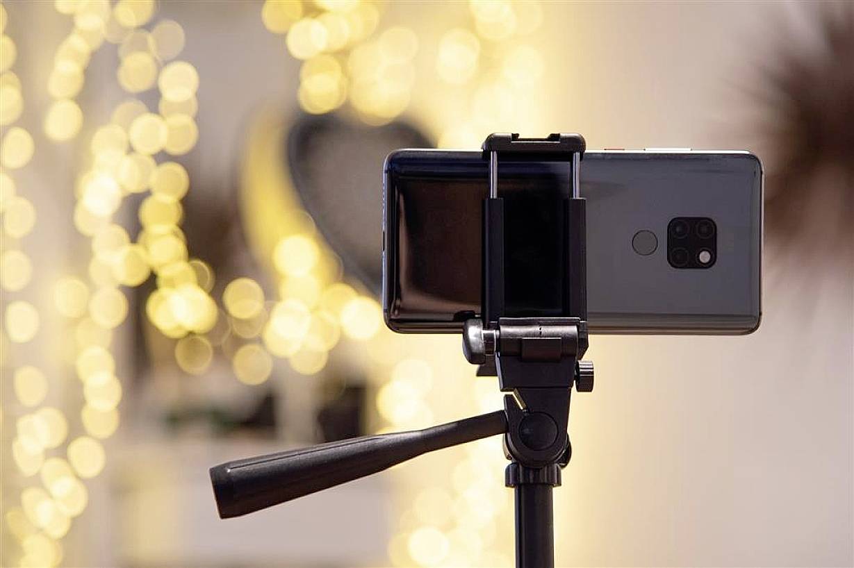 Un smartphone est fixé horizontalement sur un trépied, avec un arrière-plan présentant un effet de bokeh lumineux jaune.