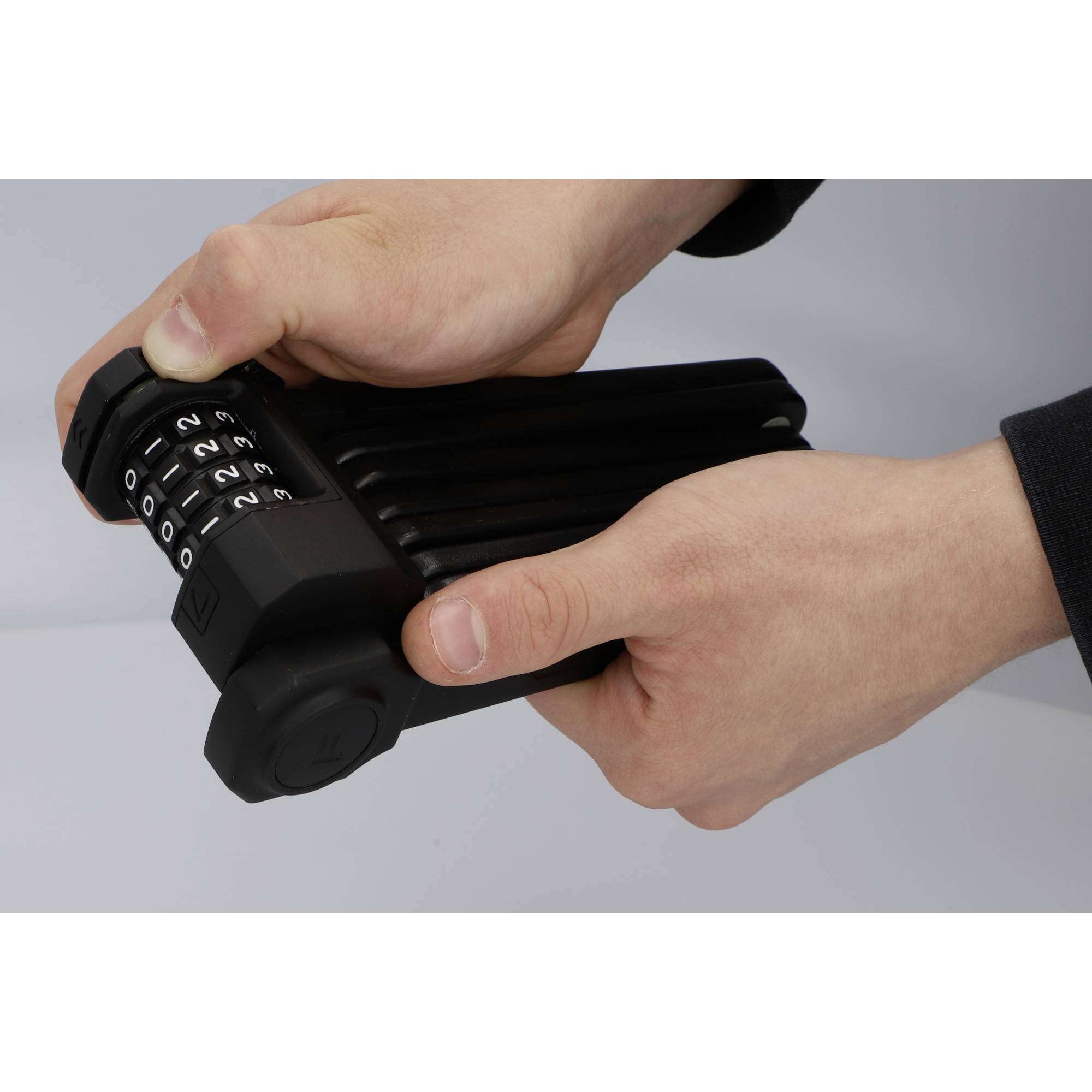 Deux mains tiennent un cadenas noir pliable à combinaison, tandis qu'une personne règle le code avec son pouce.