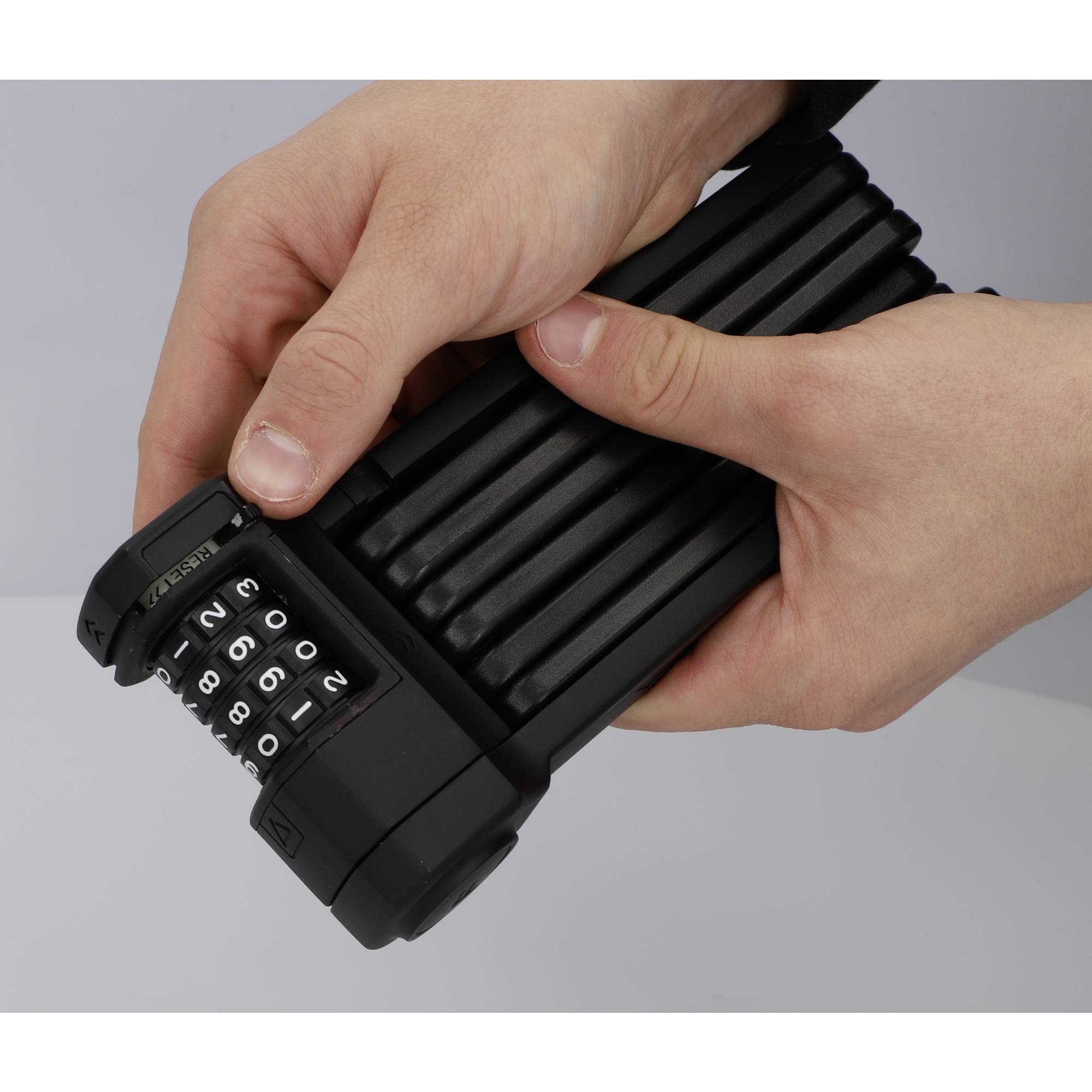 Deux mains tiennent un antivol de vélo noir et pliable avec un code numérique, le pavé numérique affichant '1250'.