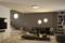 Vue d'un salon moderne avec des murs gris, des canapés confortables, une bibliothèque et une table basse centrale. Éclairage discret au plafond et sur les murs.