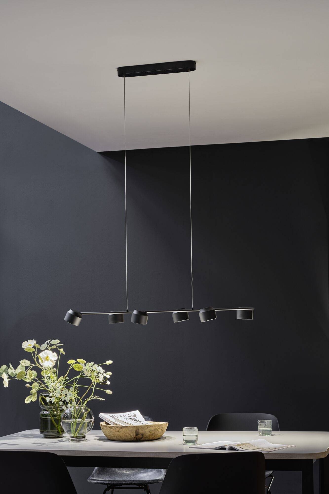 Suspension multiabat-jour suspendue au-dessus d'une table à manger moderne, avec un vase de fleurs et un bol, un mur gris en arrière-plan.