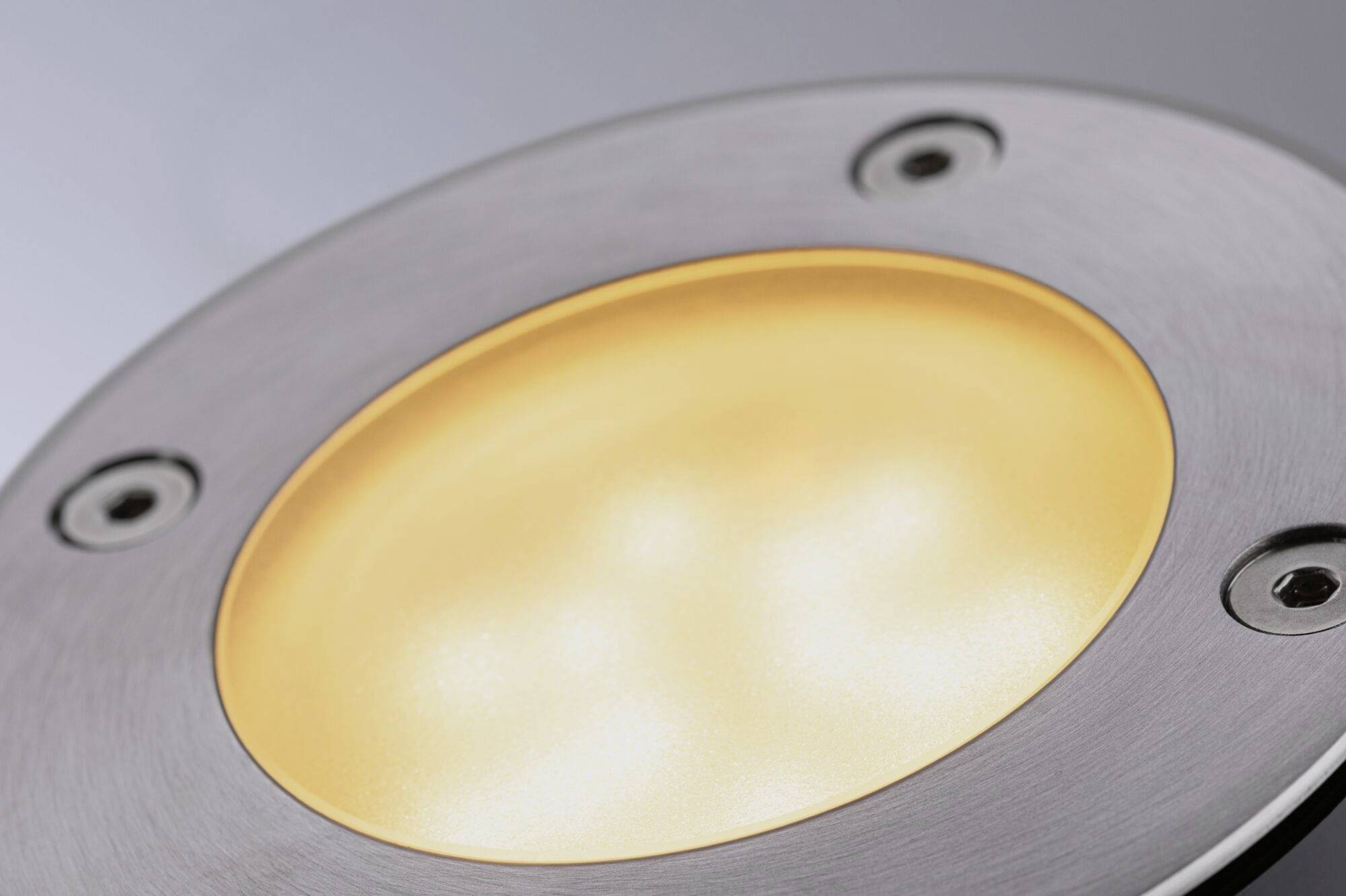 Gros plan sur un plafonnier LED rond argenté, diffusant une lumière chaude et jaune. Design d'éclairage pour intérieurs modernes.