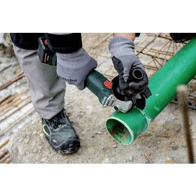 Une personne coupe un tuyau vert à l'aide d'une meuleuse d'angle. Elle porte des gants et des vêtements de protection. Environnement de chantier en arrière-plan.