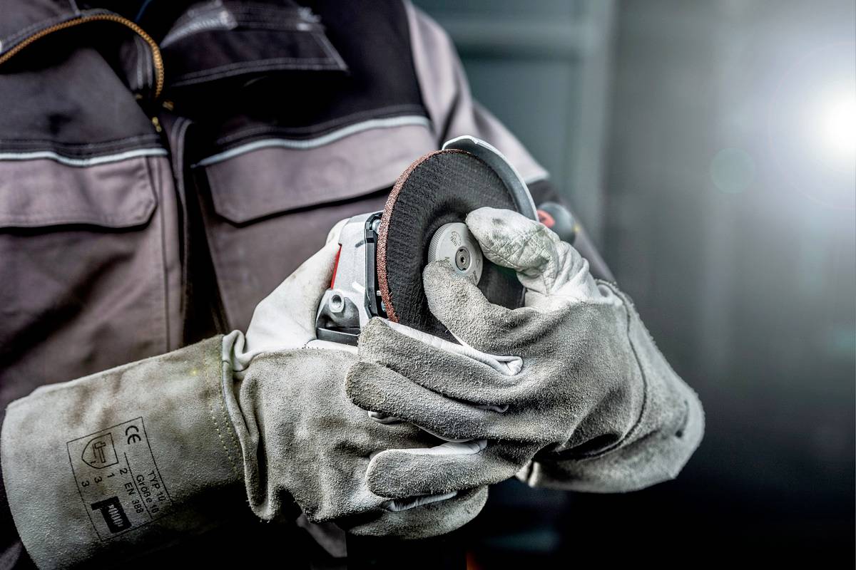 Une personne portant des gants tient et utilise une meuleuse. La mise au point est sur les mains et la machine dans un environnement de travail.