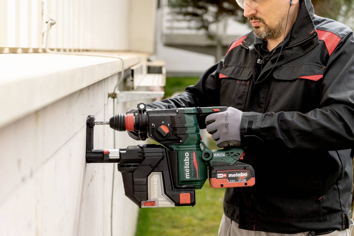 Une personne en tenue de travail utilise un marteau-perforateur électrique vert pour percer un trou dans un mur en béton.