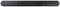 Soundbar noire, rectangulaire, aux angles arrondis, avec deux grilles de haut-parleurs visibles, posée sur une surface.
