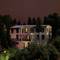 Une maison résidentielle illuminée au crépuscule, entourée d'arbres. Différentes fenêtres émettent une lumière chaleureuse.