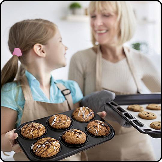 Une fille et une femme cuisinent ensemble. La fille tient un plateau de muffins, la femme tient une plaque de cookies. Elles rient.